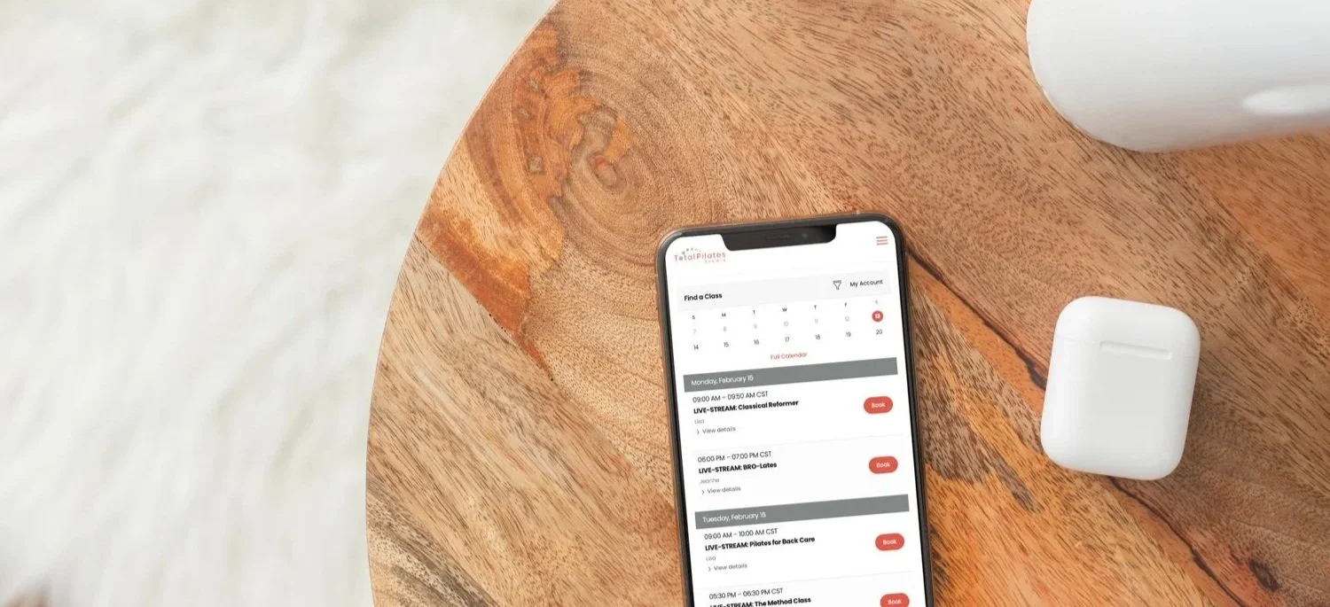 Mindbody app shown on a phone resting on a wooden table beside AirPods