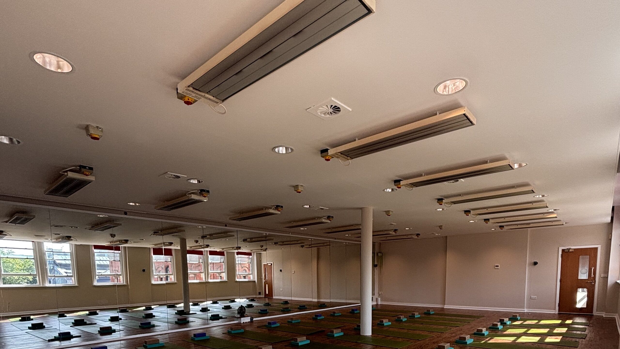 Infrared heaters across the studio ceiling at Deansgate Haus, with mats laid out beneath the windows